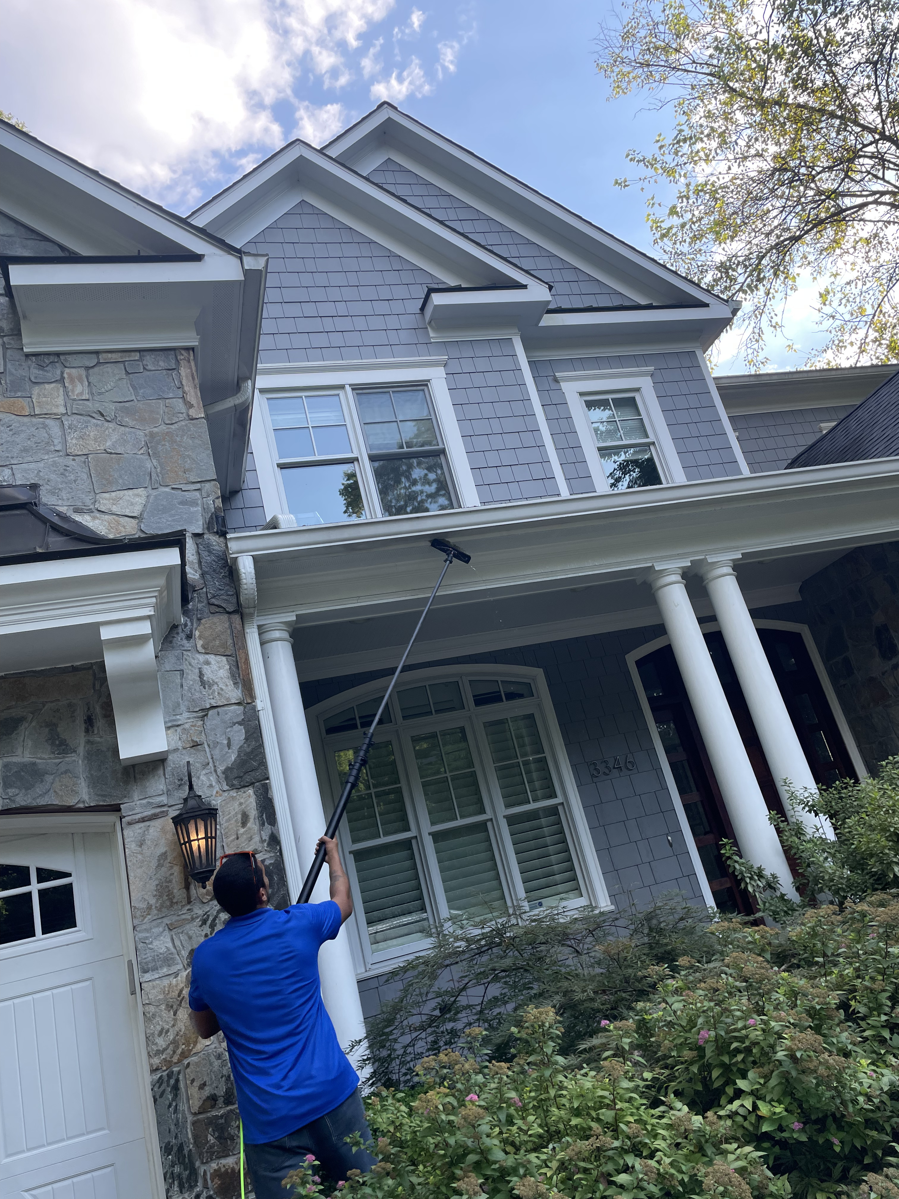 Three-person crew soft washing a tall white stucco home from the side driveway