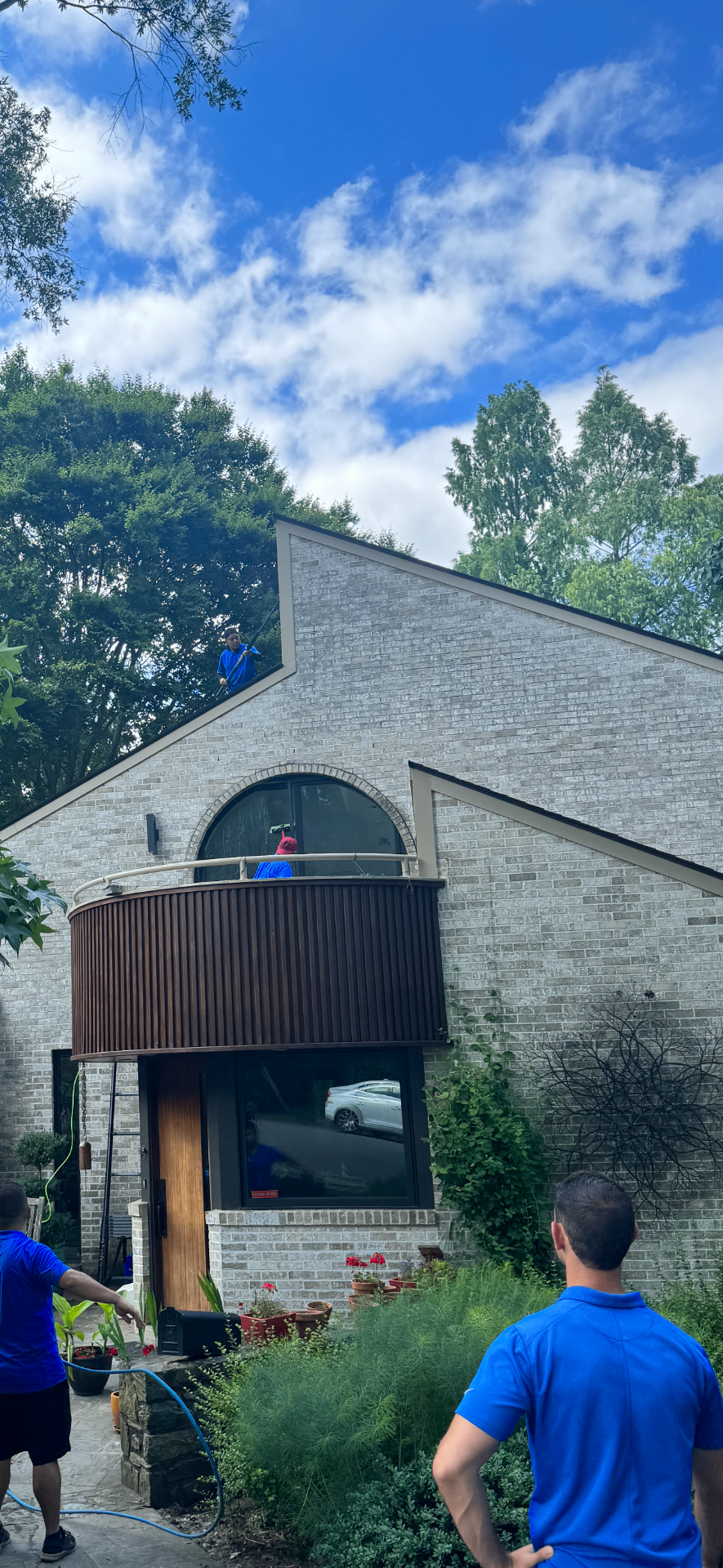 Technician using a water-fed pole to clean upper windows on a stone-and-shingle home