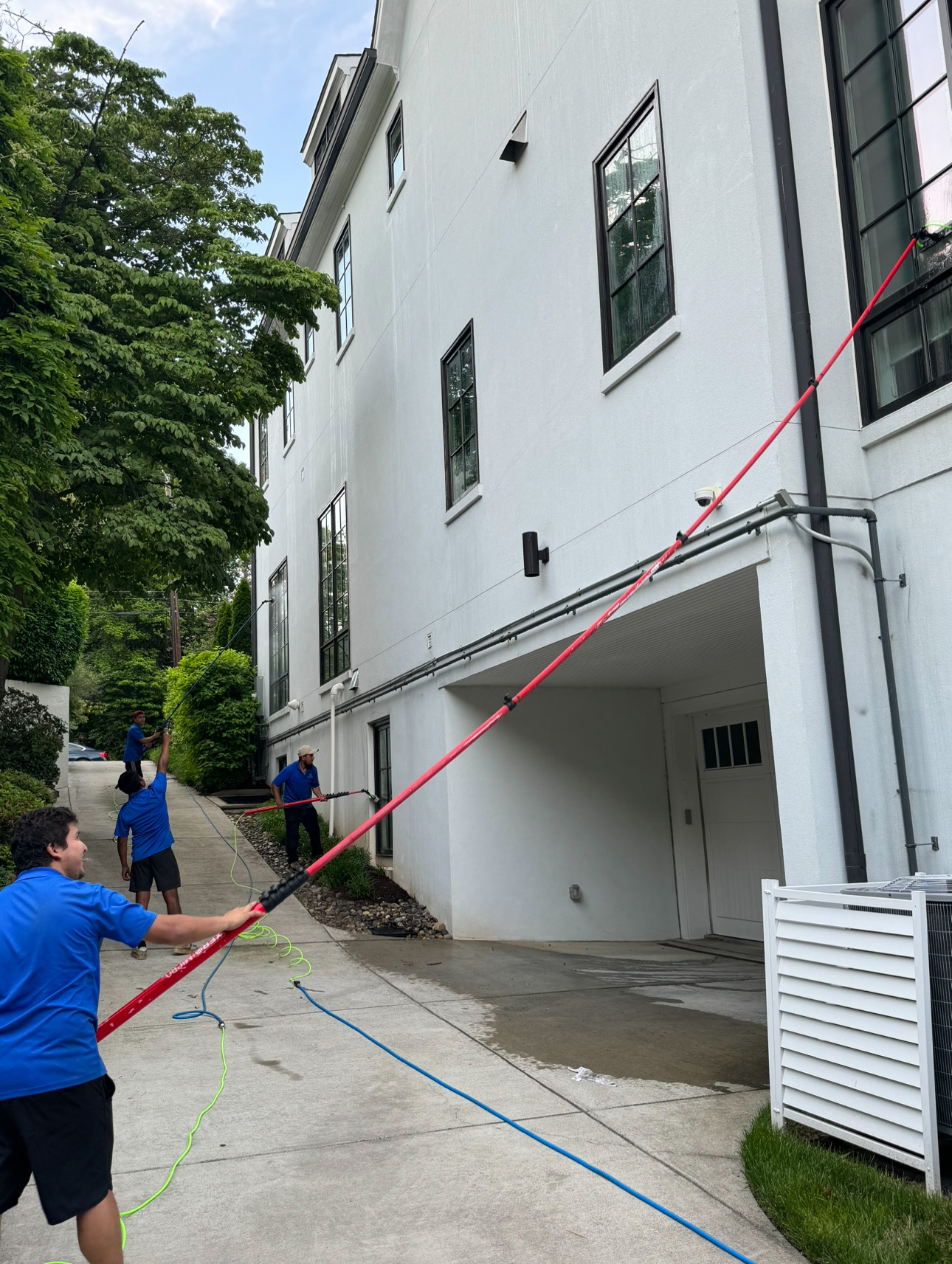 Crew using water-fed poles to soft wash a white stucco home